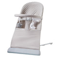 The Nuby Musical Moves Baby Bouncer Chair in beige has a quilted backrest, safety harness, and toy bar with plush cloud and star. Sturdy white metal legs provide a wide, stable base for safe bouncing fun.