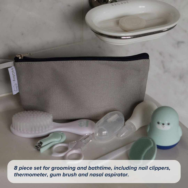 The Nuby Baby Healthcare and Grooming Kit, in a gray zippered pouch, includes a brush, nail clippers, thermometer, gum brush, nasal aspirator, and a blue penguin-shaped item—displayed on a white surface.