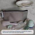 The Nuby Baby Healthcare and Grooming Kit, in a gray zippered pouch, includes a brush, nail clippers, thermometer, gum brush, nasal aspirator, and a blue penguin-shaped item—displayed on a white surface.