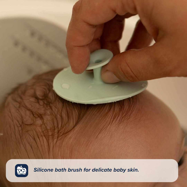 A hand gently uses a soft, round silicone brush on a baby's head. Text below reads: Nuby Baby Healthcare and Grooming Kit—includes a silicone bath brush, essential for caring for delicate newborn skin.