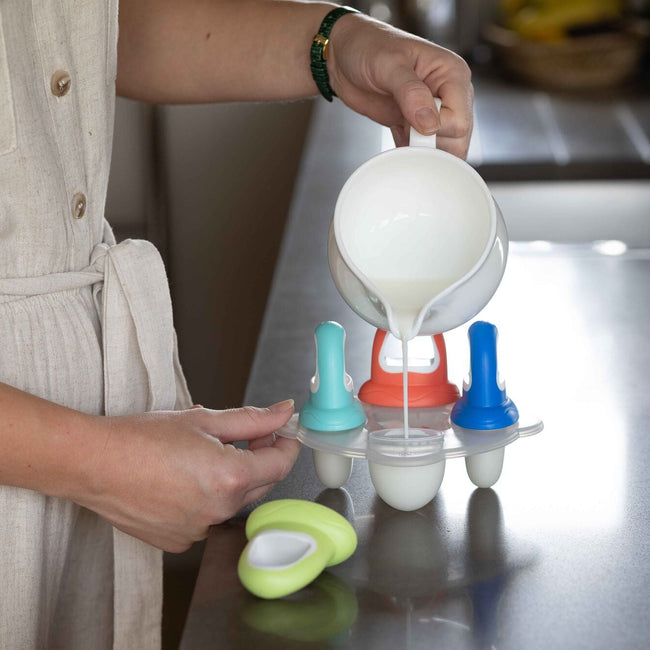 The set of fruitsicles ice pop tray having milk poured into them on a kitchen counter top. A product by Nuby.