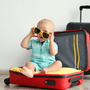 newborn essentials blog cover including a baby wearing sunglasses and being sat inside a suitcase.
