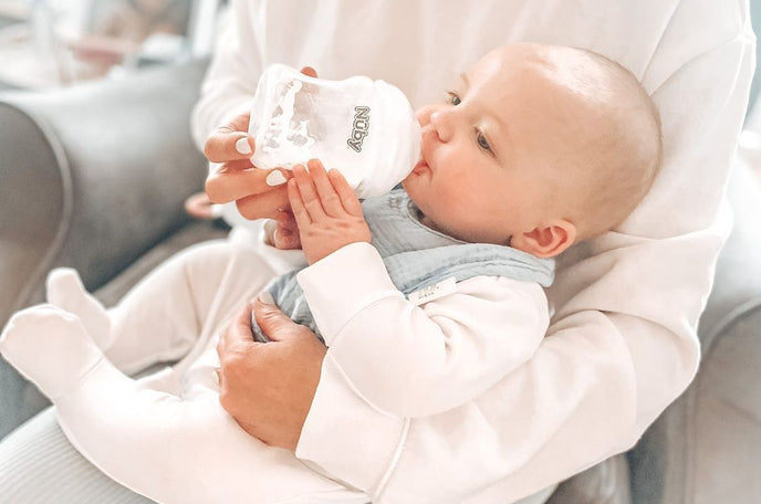 A baby drinking from a Nuby bottle while in their parents' arms.