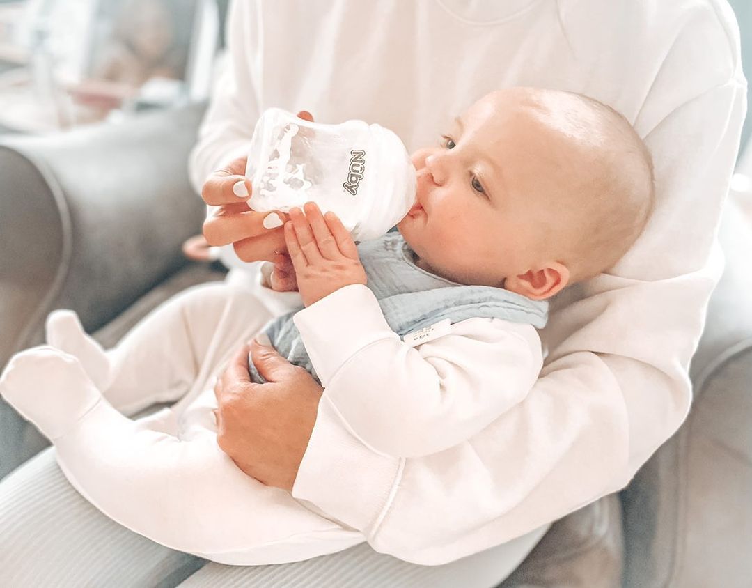 A baby drinking from a Nuby bottle while in their parents' arms.