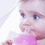 A baby drinking from a Nuby bottle that has a pink top. They are looking away from the camera while drinking.