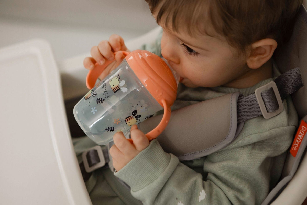 A baby holding a bee decorated sippy cup to their mouth to drink from.