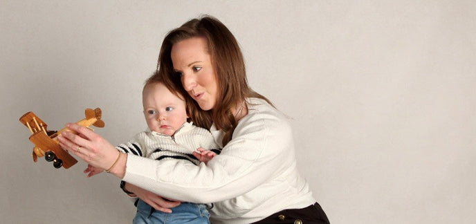 A woman holding a toy plane in front of their baby child who is staring at the plane.