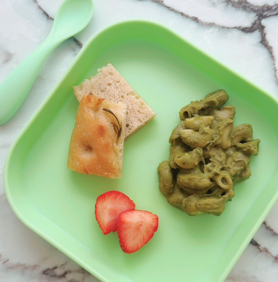 A plate with pasta, focaccia bread and strawberries placed upon it. The plate is green.