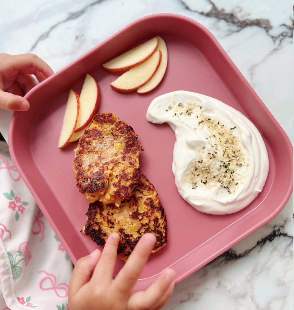 Sweet potato burgers sat on a pink plate created by Nuby, this is accompanied by sauce and apple slices.