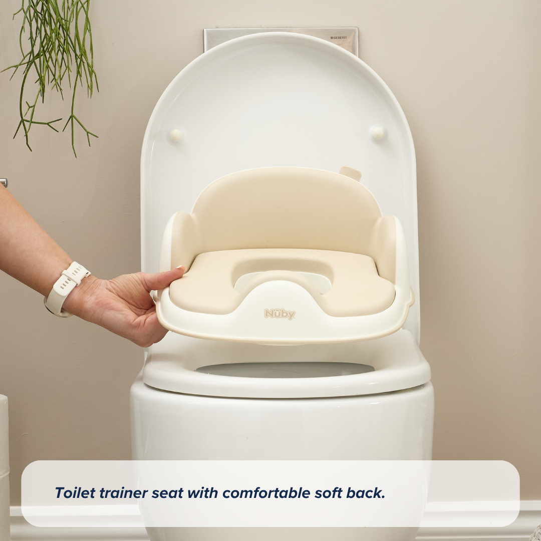 A hand places the Gro Up 3 in 1 Potty, featuring a cushioned trainer seat with a soft back, onto a white toilet—perfect for potty training—set against a beige wall with a hanging plant nearby.