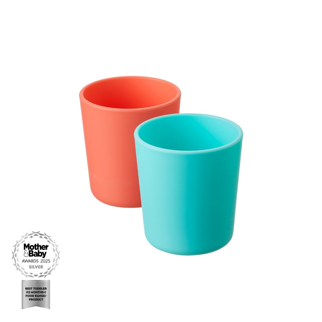 Two Nuby Toddler Tumblers 2 Pack, one coral and one teal, sit side by side on a white background. A silver Mother & Baby Awards 2025 badge is in the lower left corner. Ideal as a weaning cup for little ones from Nuby.