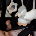 A close-up of a babys hand reaching for the Nuby Penguin Activity Spiral Travel Pram Toy, featuring a gray penguin and hanging soft star and cloud, all attached to a car seat handle.