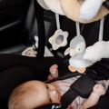 A baby lies in a car seat, safely buckled in and looking up at the Nuby Penguin Activity Spiral Travel Pram Toy—a soft, plush toy featuring cute animal characters hanging overhead.
