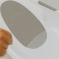A close-up shows the Nuby Newborn Baby Bath—a white tub with a gray, non-slip mat and Nuby embossed. Part of a childs arm appears in the lower left. Ideal for safe newborn bath time.