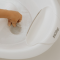 A hand presses on a gray suction pad inside the white Nuby Sit Me Up Baby Bath, with the brand name visible on the rim, ensuring secure support for newborns during bathing.