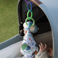 A baby in a stroller outdoors reaches for Nuby Linkables toys with beads and fabric attached to the canopy, partially covered by a blanket.