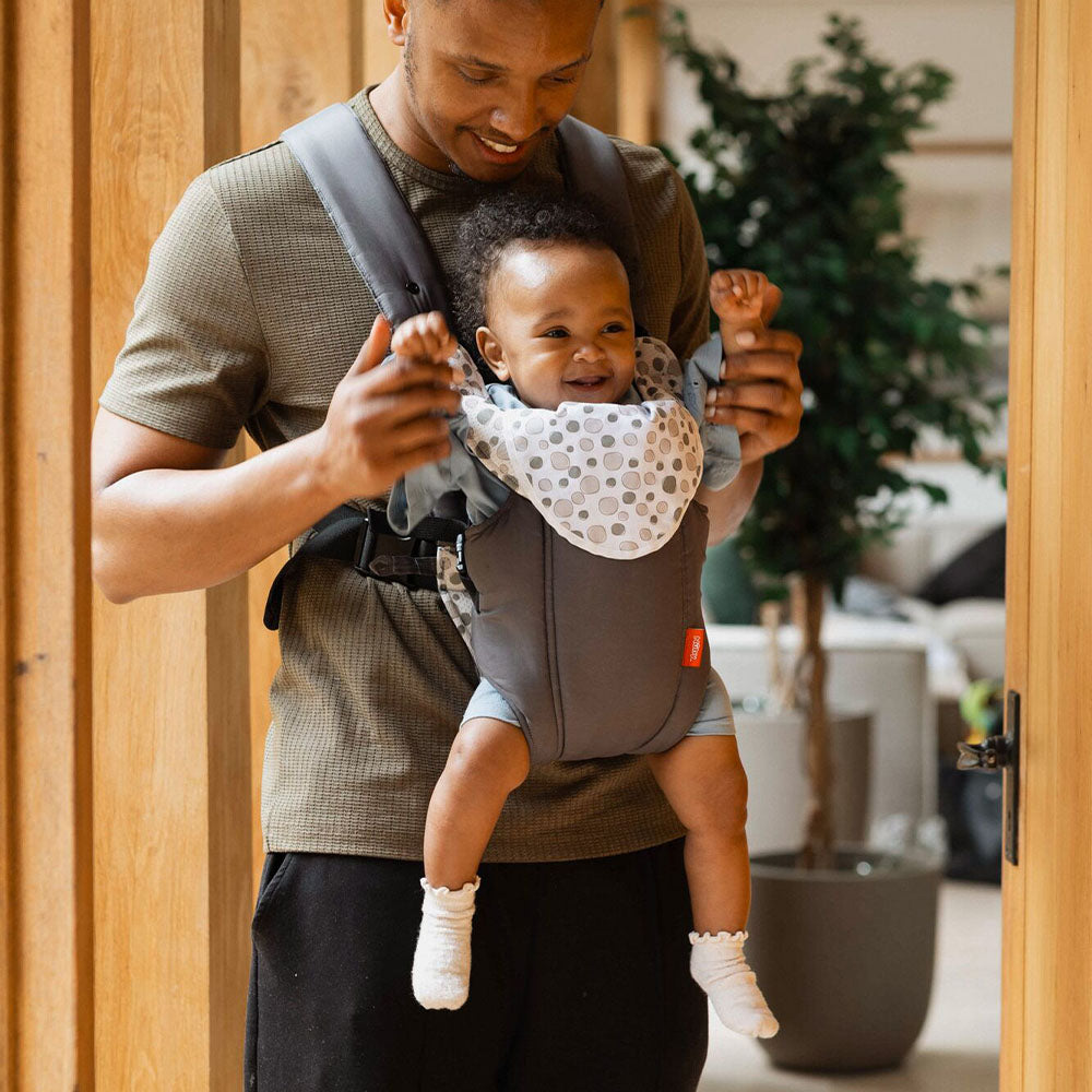 A baby with their arms raised while i nthe 2 in 1 Baby Carrier by Nuby. Their Father is looking at them and interacting with them while they are using the carrier.