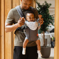 A baby with their arms raised while i nthe 2 in 1 Baby Carrier by Nuby. Their Father is looking at them and interacting with them while they are using the carrier.