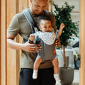 The 2 in 1 Baby Carrier by Nuby. A baby is sat inside the carrier while their Father is holding the baby with this device. Both of them are smiling.