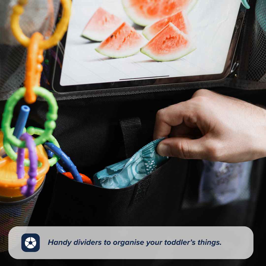 A hand places an item into a Nuby Car Seat Organiser pocket, which also holds colorful rings and a cup. Above, a tablet shows watermelon slices. Text: Handy dividers to organise your toddler’s things for easy travel storage.