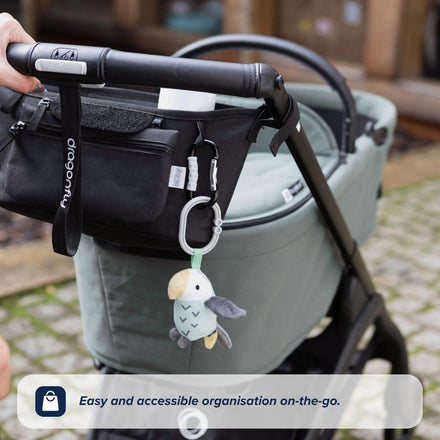 A close-up of a stroller with the Nuby UK Pushchair Essentials Kit—featuring a black organiser on the handle and a soft bird toy clipped on. Text reads: Convenient organisation for your pushchair must-haves.