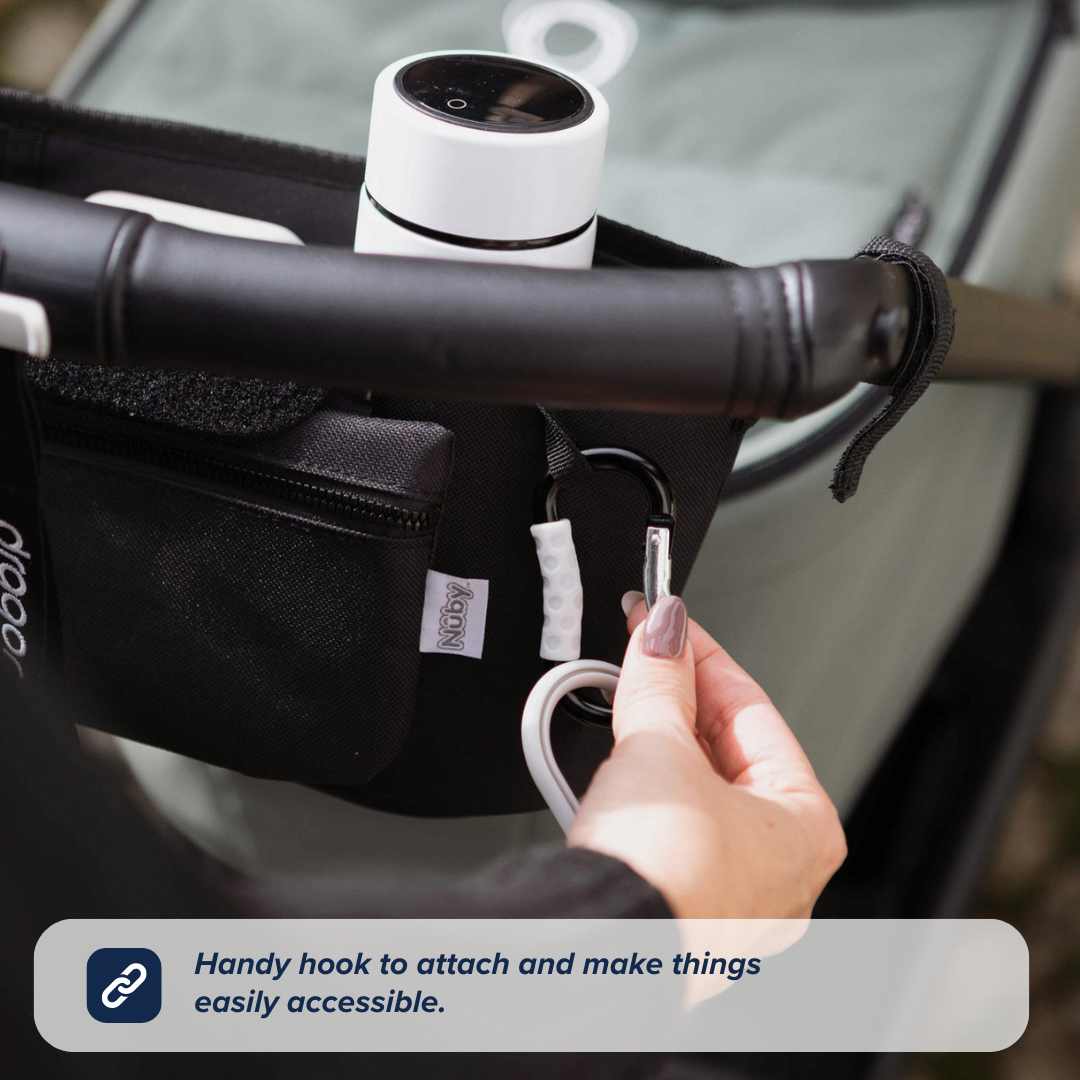 A hand attaches a white carabiner hook to the black Nuby Pram Organiser Bag, which holds a cup and a zippered pouch, with a label reading: “Handy hook to attach and make things easily accessible.”.