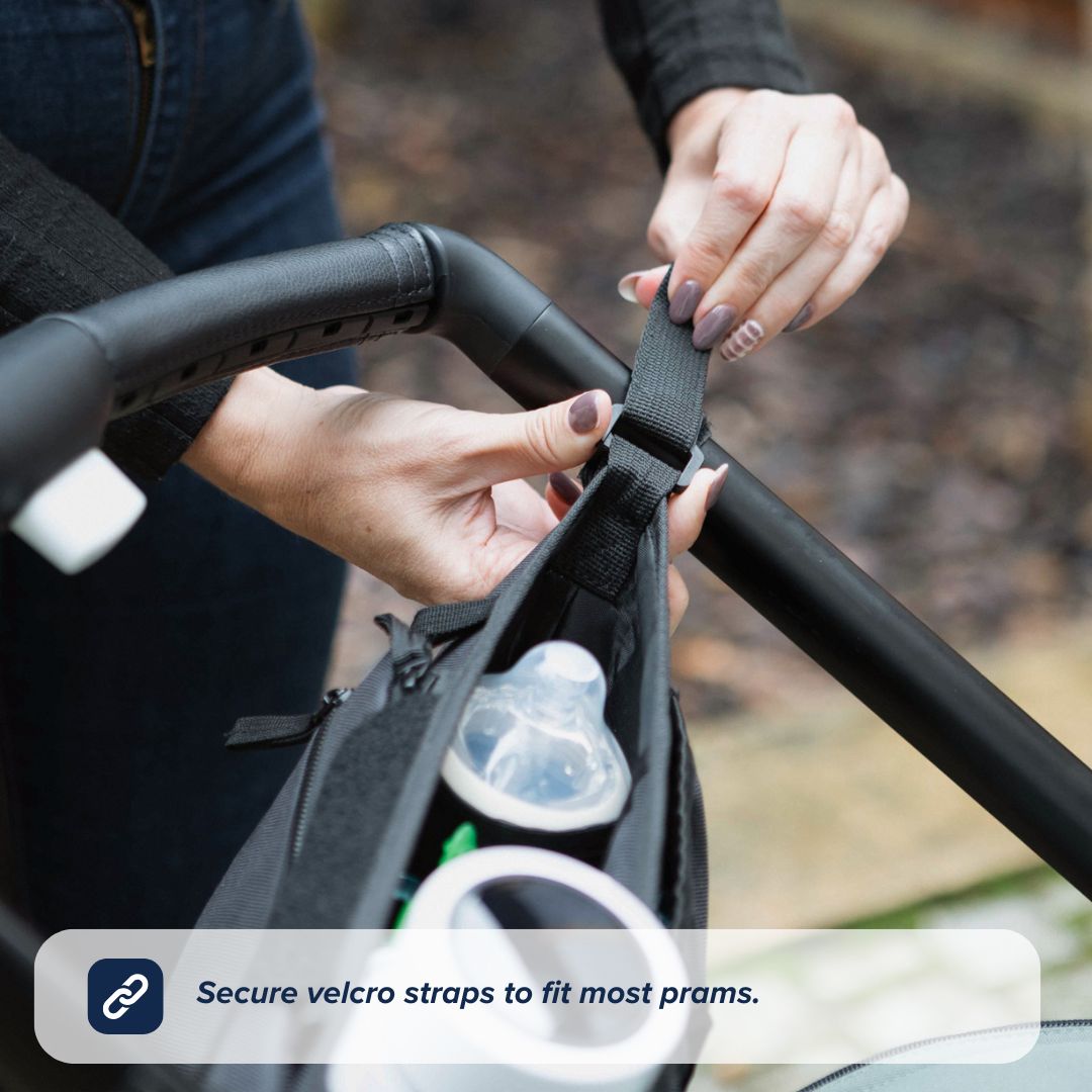 A person attaches the Nuby UK Pushchair Essentials Kit, a black organiser, to a stroller handle using secure velcro straps. The organiser holds a baby bottle and more. Text overlay: Secure velcro straps fit most prams.