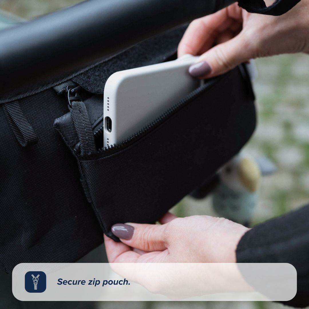 A person puts a white smartphone into the secure zip pouch of the black Nuby UK Pushchair Essentials Kit attached to a stroller handle. Text overlay: Secure zip pouch.
