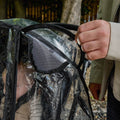 A person opens a mesh vent on a clear plastic Pram Rain Cover, with a small child partially visible inside. Trees and a wooden fence are blurred in the background.