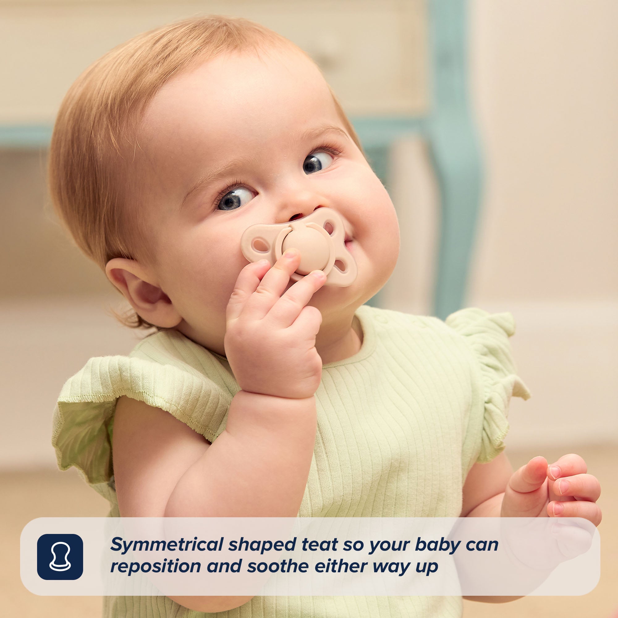 A baby in a light green outfit holds a beige silicone dummy near their mouth. Text reads: The RapidSoother 2-pack of Dummies features a symmetrical shaped teat, allowing your baby to reposition and soothe either way up.