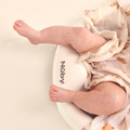 A baby wrapped in a white blanket with bear prints sits in a Newborn Baby Bath Support featuring a cushioned back rest, with only their legs and part of the blanket visible.