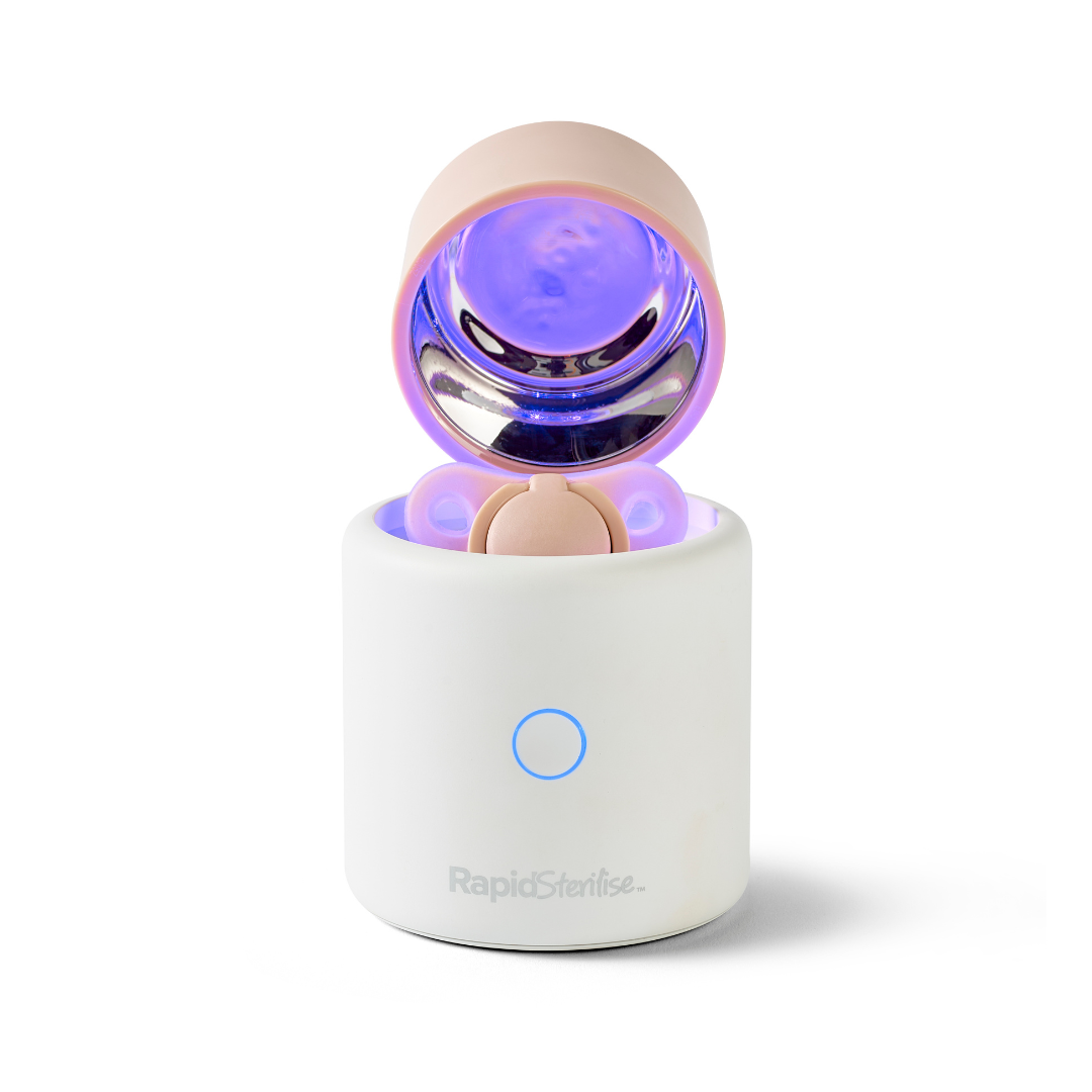A white cylindrical RapidSoother Dummy & Pod with a pink rounded lid open, showing a glowing purple interior. It features a blue power button and has the RapidSoother logo on the front.