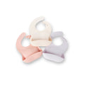 The Silicone Bibs 3 Pack features pastel peach, cream, and lavender bibs arranged overlapping on a white background. Each has an adjustable neck and deep front pocket to catch food.