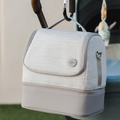 A gray insulated cooler bag hangs from a stroller handle, paired with the Nuby UK RapidCool Twin Pack and Portable UV Steriliser Bundle. This setup keeps bottles ready on the go. The backdrop includes part of the stroller and some grass.