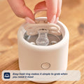 A hand lifts a RapidSoother dummy by its easy-hold ring from a compact sterilizer on a wooden surface. Caption reads: Easy-hold ring makes it simple to grab your RapidSoother silicone dummy when you need it most.