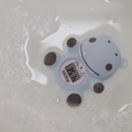 The Nuby Hippo Bath & Room Thermometer, shaped like a blue hippo, floats in soapy water. Its digital display reads 36.1°C as bubbles surround the cheerful thermometer.