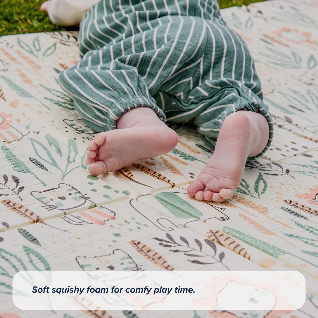 A baby in green striped pants lies outdoors on the Fold N Go Play Mat, which features a patterned, non-slip surface. Text at the bottom reads, Soft squishy foam for comfy play time.