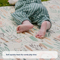 A baby in green striped pants lies outdoors on the Fold N Go Play Mat, which features a patterned, non-slip surface. Text at the bottom reads, Soft squishy foam for comfy play time.