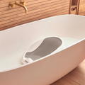 A white bathtub filled with water features the Newborn Baby Bath Support, equipped with a cushioned backrest for your baby’s comfort. In the background, a wooden wall with a gold faucet and a storage basket can be seen, while the built-in max water level indicator on the bath support ensures safe and comfortable bathing for your little one.
