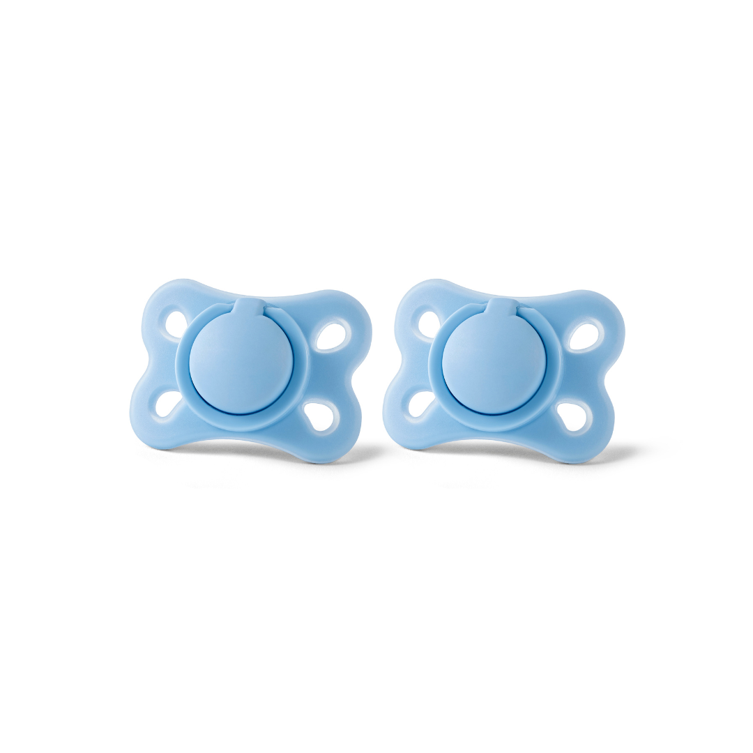 Two RapidSoother light blue newborn dummies, each with a rounded knob and four ventilation holes on each side, are placed side by side on a white background.