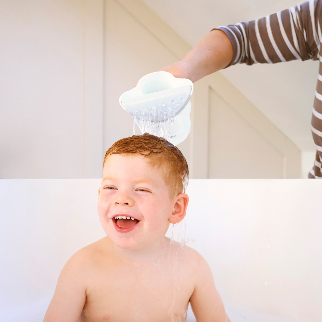 A happy toddler sits in the tub while an adult gently pours water over their head with the Shampoo Rinse Pail. The brightly lit background highlights this cheerful bath time moment.
