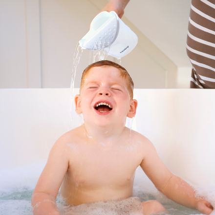 A young child smiles with eyes closed while an adult uses the Shampoo Rinse Pail to gently pour water over their head, creating bubbles and making bath time full of joy and laughter.