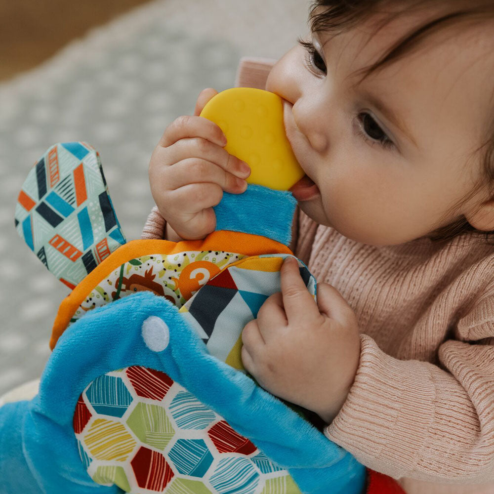 A baby chewing the teether book with blue decorations on the outside.