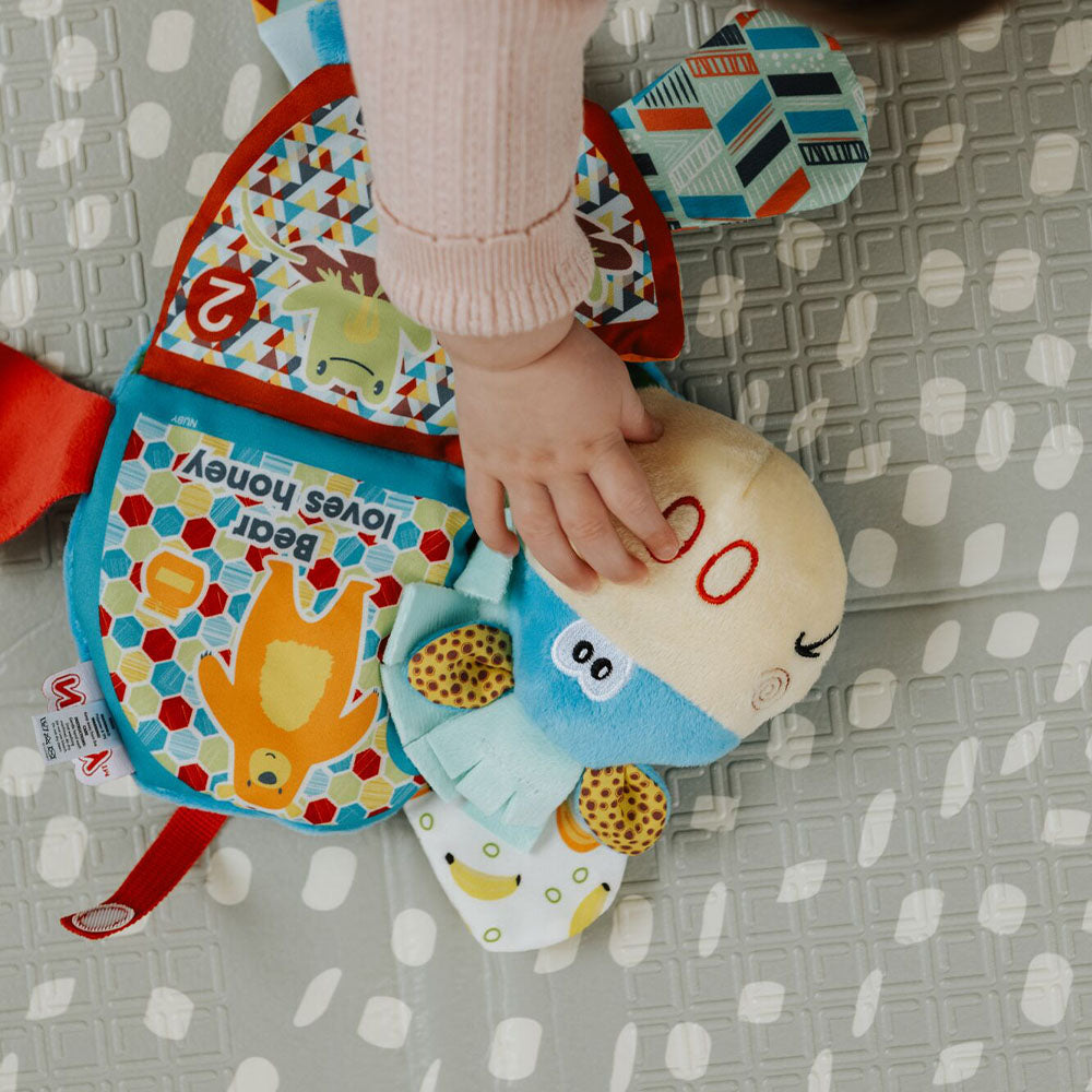 A baby reaching for the face of an animal that is included in the Teether book by Nuby.