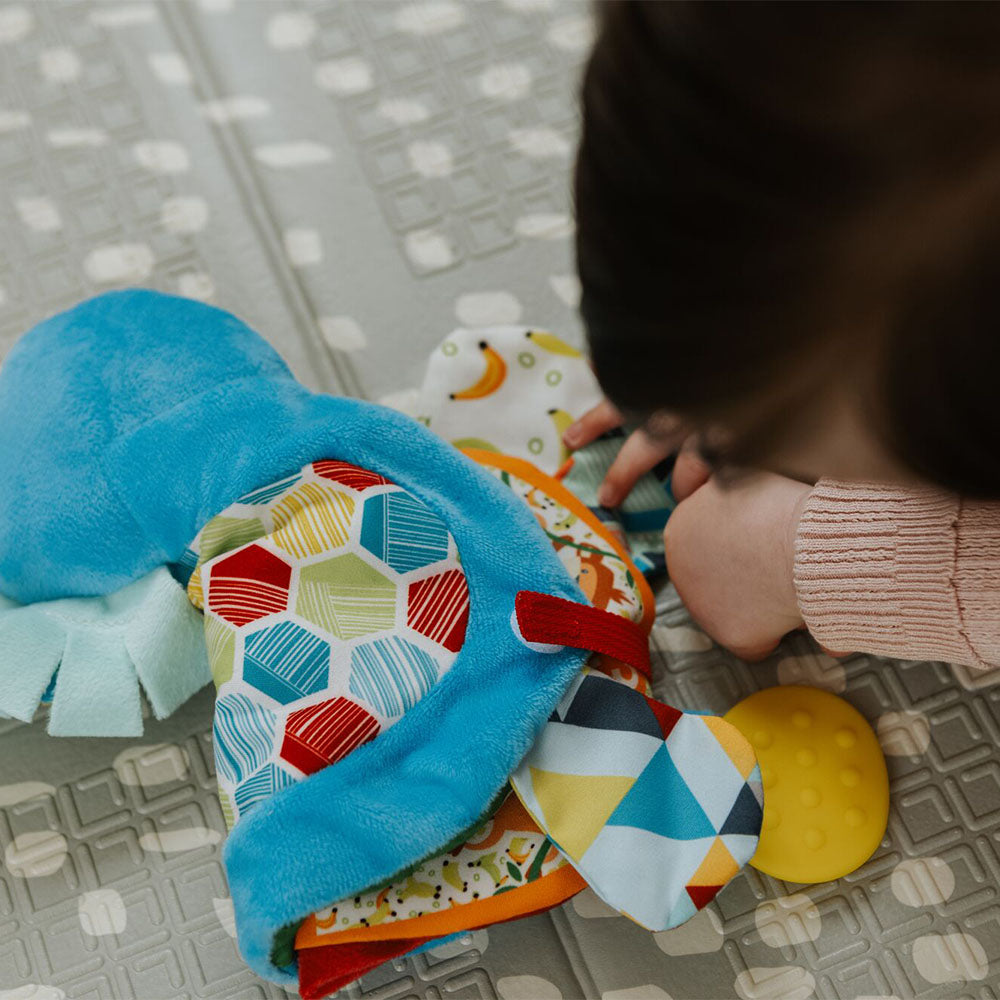 A baby playing with a teether book from Nuby.