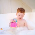 A young child with red hair sits in a bubble-filled bathtub, enjoying water play with the Fun Watering Can.