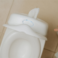 The Nuby My Real Mini Toilet Potty, featuring a built-in wipe dispenser, sits on a tiled floor as a child’s hand enters the frame—capturing an engaging toilet training moment.