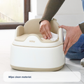 A person wipes a Gro Up 3 in 1 Potty in beige and white with a cloth. The potty trainer sits on a white tile floor near a window. Text at the bottom reads, Wipe clean material.