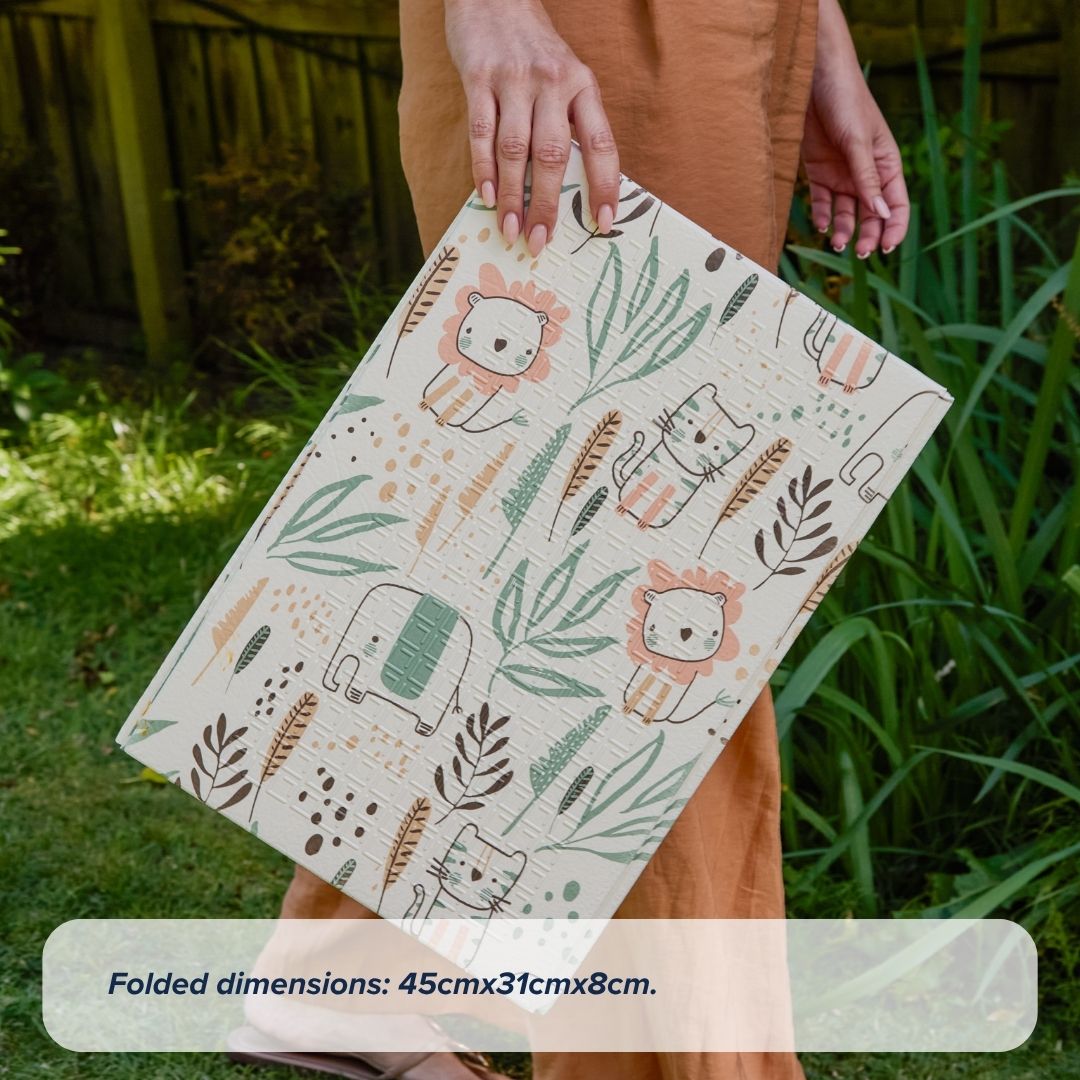 A person holds a Fold N Go Play Mat featuring playful cartoon lions, elephants, and plants. The beige, foldable play mat is accented with green and orange. Text below reads: Folded dimensions: 45cm x 31cm x 8cm.