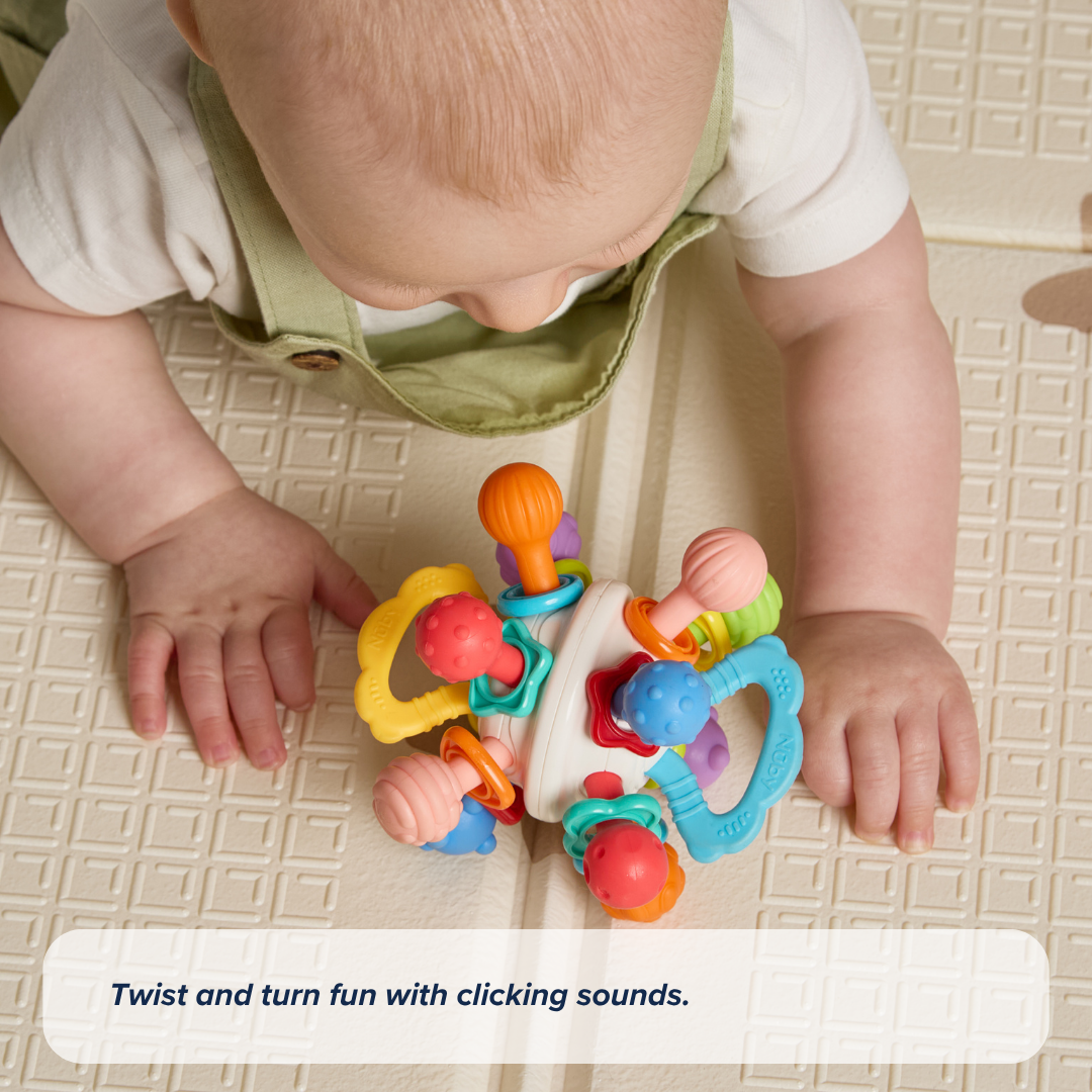 A baby in green overalls plays with the Twist Ball Teether on a textured mat. Text at the bottom reads, Twist and turn fun with clicking sounds.